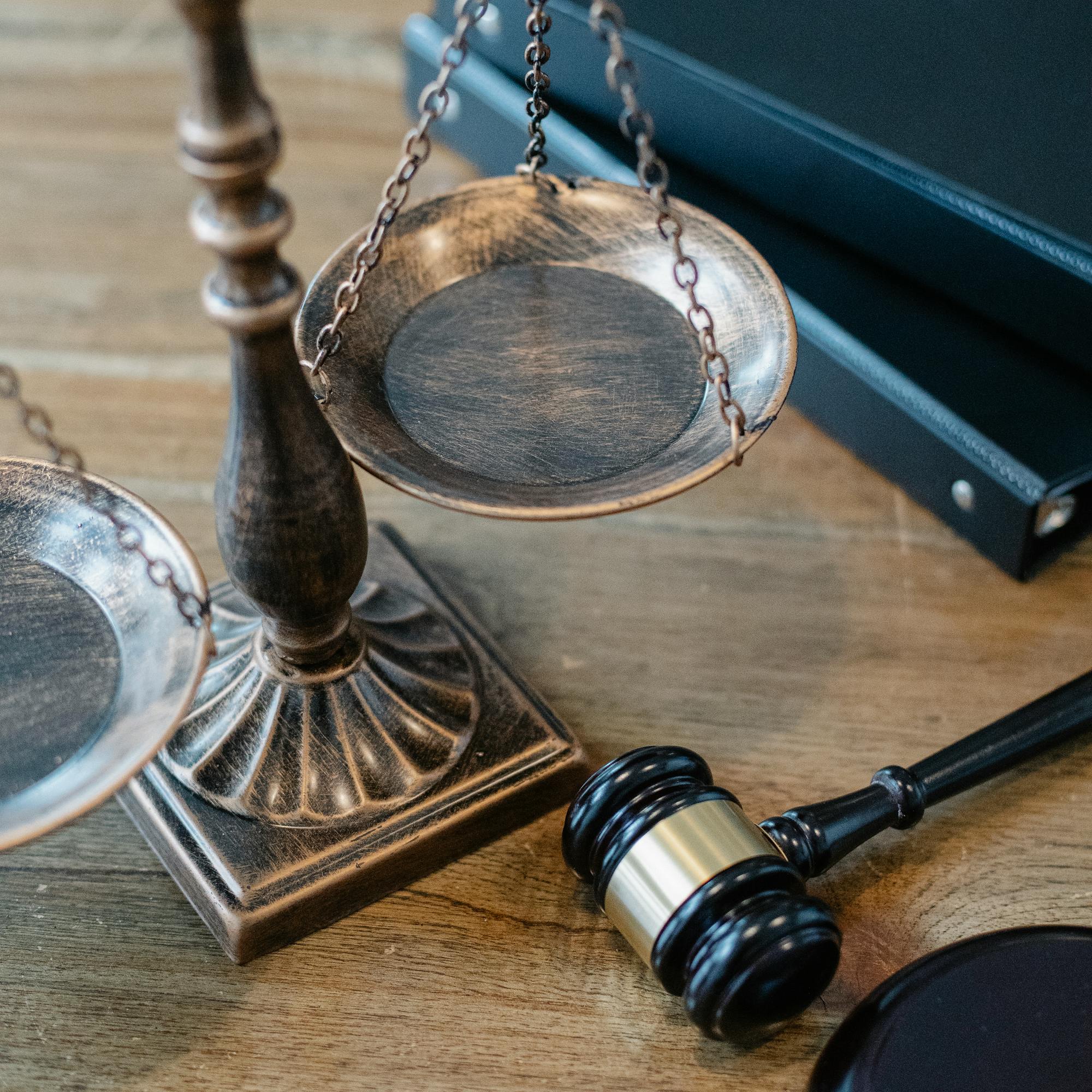 Balança da justiça e martelo institucional sobre superfície de madeira escura — referência simbólica à jurisdição trabalhista.